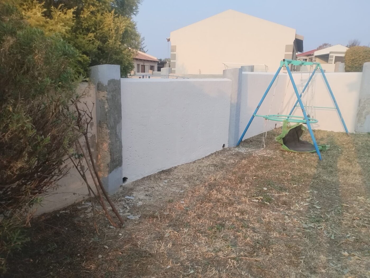 Newly painted white boundary wall with one section awaiting the finish coat.