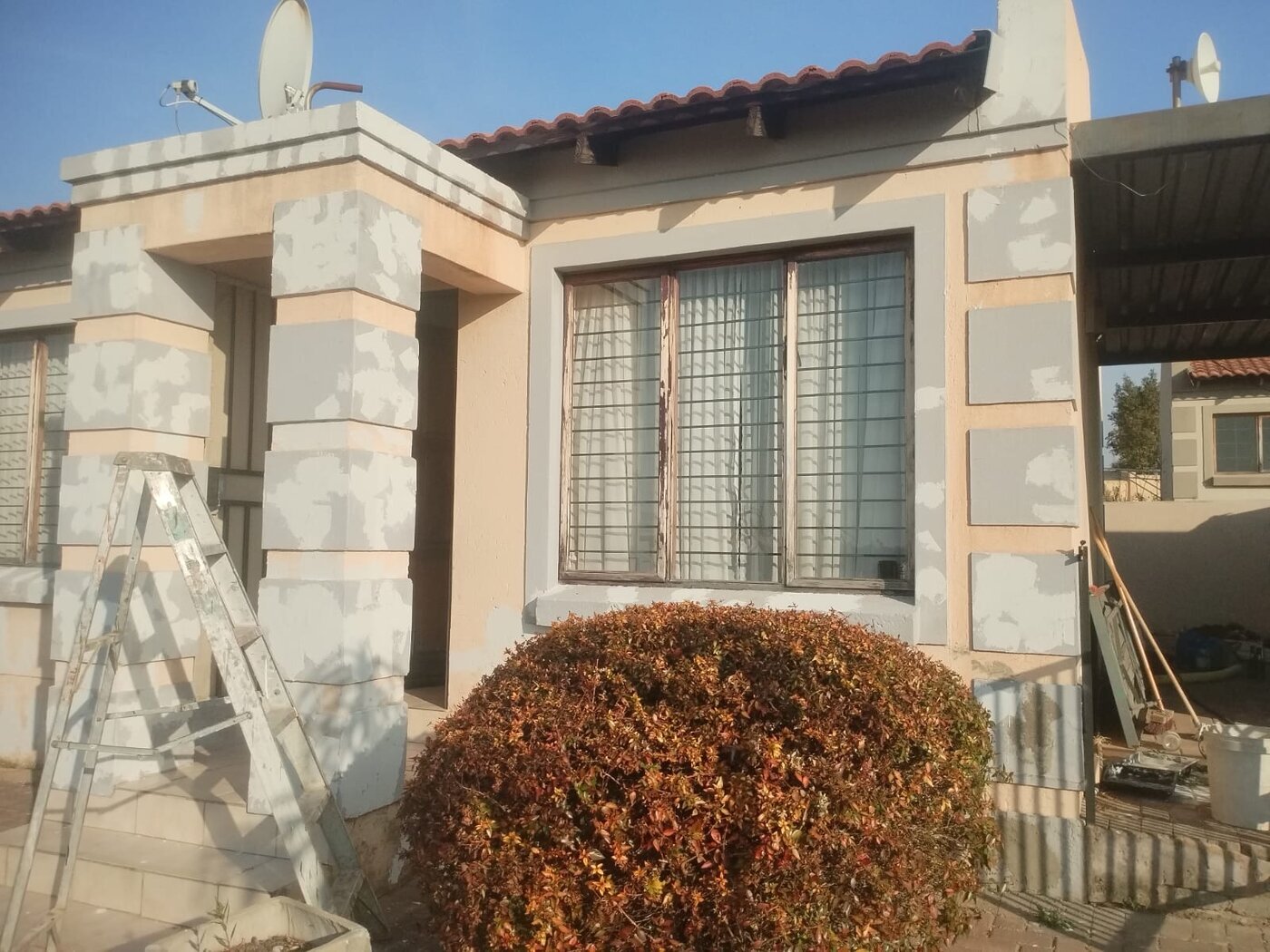 Home exterior painting underway with ladder and supplies at the entrance.