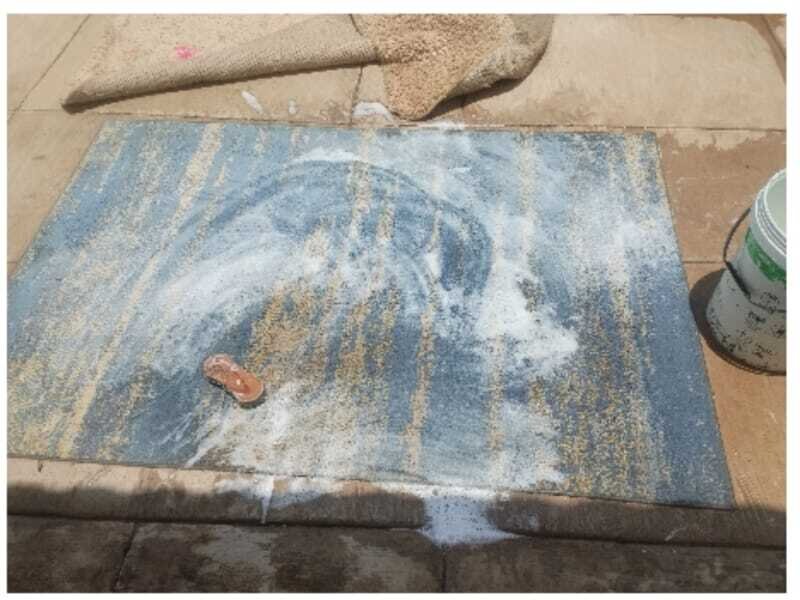 Patterned rug deep cleaned with foam and brush on a patio.