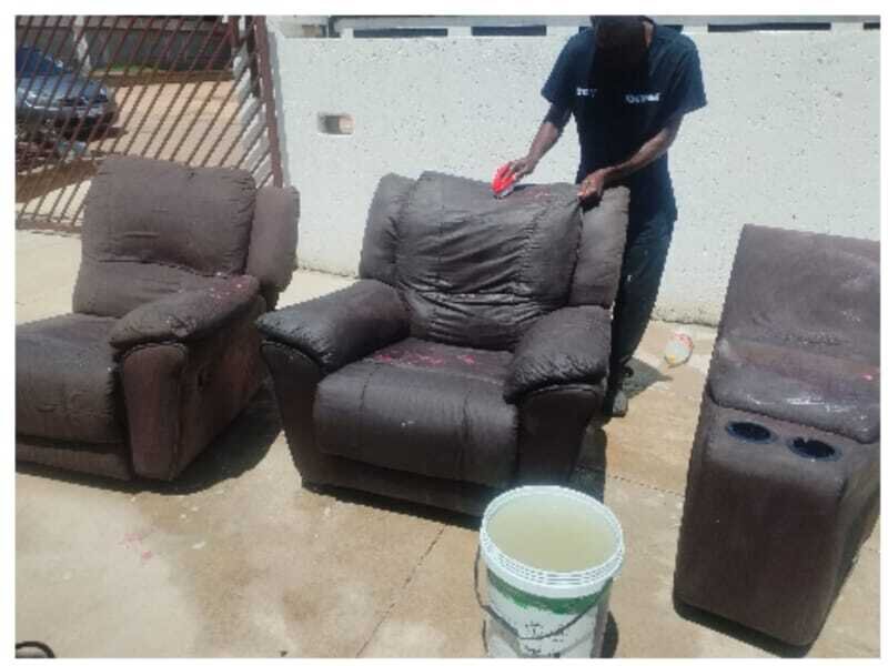 Technician hand-scrubbing a brown reclining sofa during outdoor deep cleaning.