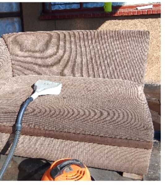 Extraction tool deep-cleaning brown fabric sofa cushions outdoors.