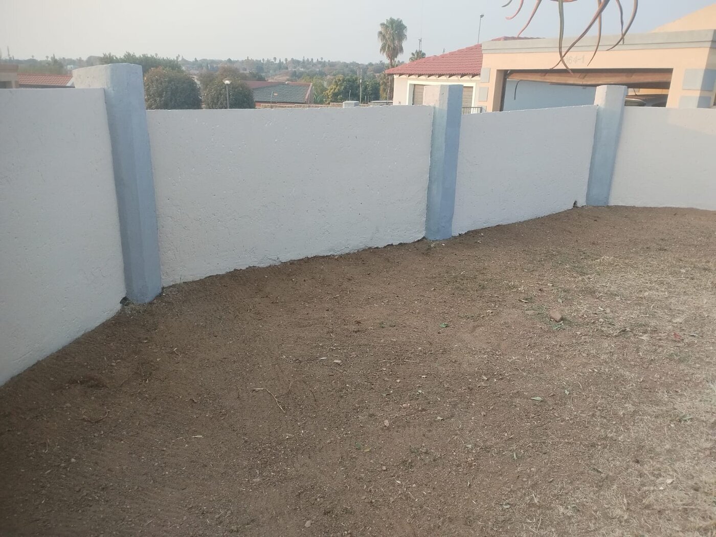Cleared yard alongside a freshly painted white and grey perimeter wall.